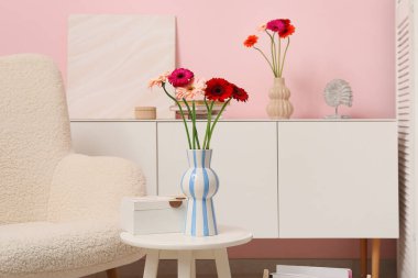 Koltuk, çekmece sandığı ve oturma odasının içinde vazoda Gerbera çiçekleri olan kahve masası. Yakın çekim.