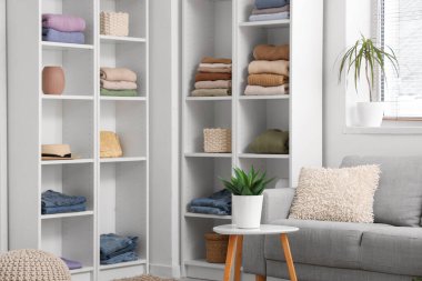 Aydınlık odada katlanmış elbiseli ve çiçekli raflar.