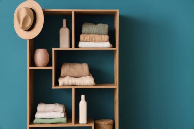 Katlanmış elbiseli ahşap raf ünitesi, renk duvarının yanında şapka ve dekor.