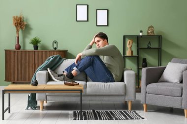 Evdeki kanepede oturan bunalımlı genç adam.