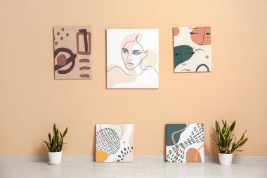 Sanat galerisinde bej duvarın yanında bitkiler olan güzel tablolar.