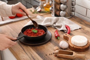 Mutfaktaki masada kepçeyle tavada domates ezmesi karıştıran genç kadın.