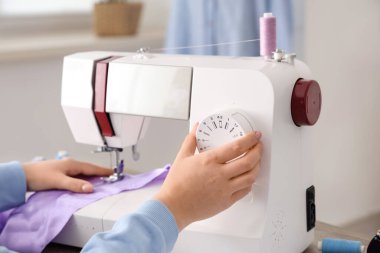 Genç bayan terzi atölyede, yakın plan masadaki leylak kumaş için dikiş makinesi kullanıyor.