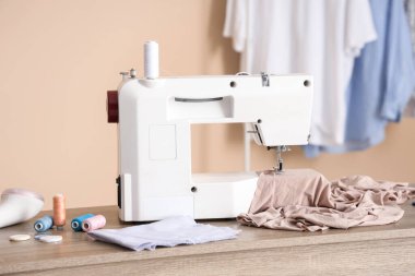Bej kumaşlı modern dikiş makinesi ve atölyedeki terzi malzemeleri.