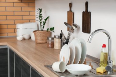 Temiz tabaklar, deterjan ve lavabonun yanında ahşap mutfak tezgahının üstünde sünger.