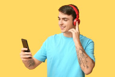 Sarı arka planda kulaklığı ve cep telefonu olan yakışıklı bir genç.