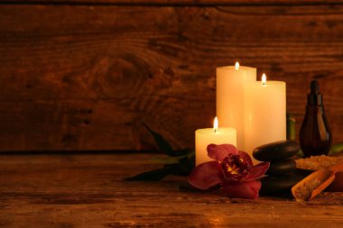 Koyu ahşap masa üzerinde yanan mumlar ve orkide çiçekli spa kompozisyonu