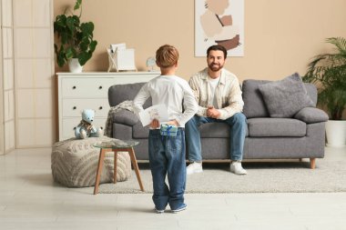 Küçük çocuk evde babasına hediye ve tebrik kartı saklıyordu. Babalar Günü.