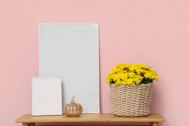 Kasımpatı çiçekleri ve tablolarla dolu sepet pembe arka planda.