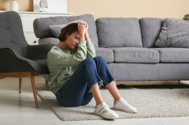 Depresyondaki genç kadın oturma odasında yerde ağlıyor.