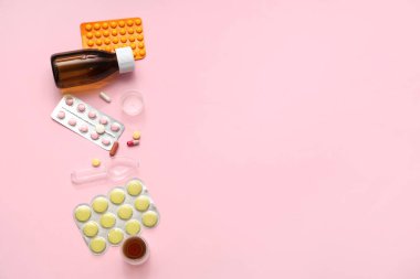 Ölçme kabı, kaşık ve pembe arka planda farklı haplarla dolu bir şişe öksürük şurubu.