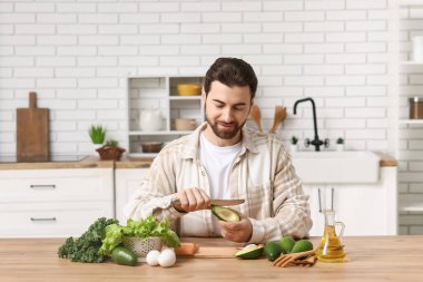 Avokado soyan sakallı genç bir adam ve mutfak masasında sağlıklı yiyecekler.