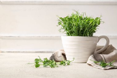 Seramik fincanda taze mikro yeşil lahanalar ve ışık masasında peçete var.