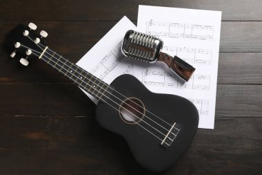 Koyu ahşap arka planda Ukulele, mikrofon ve müzik kağıtları