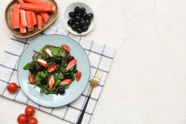 Yengeç çubuklu bir tabak salata, ıspanak, siyah zeytin ve beyaz arka planda domates.