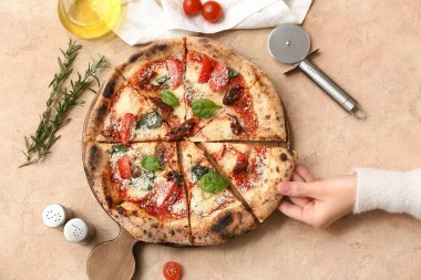 Kadın eli, bej arka planda lezzetli bir pizza dilimi alıyor. Üst görünüm