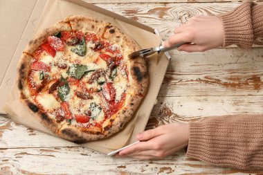 Beyaz ahşap arka planda pizza kesen kadın eller. Üst görünüm