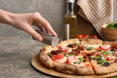 Gri arka planda lezzetli pizzaya baharat ekleyen bir kadının eli