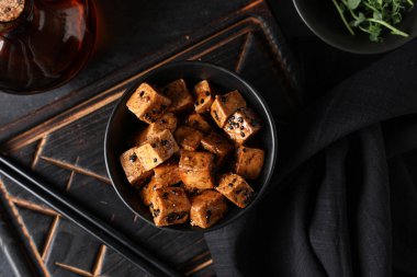 Siyah zemin üzerinde kızarmış tofu peyniri parçaları olan bir kase.