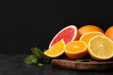 Farklı turunçgil meyveli ahşap tahta ve siyah arkaplanlı nane.