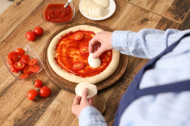 Mutfak masasının yanındaki pizzaya mozzarella peyniri koyan kadın.