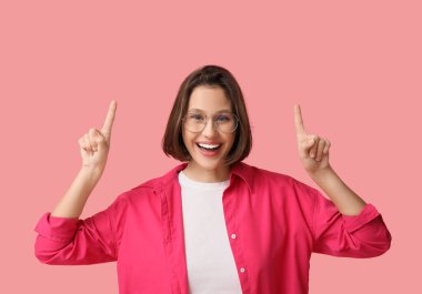 Güzel genç bir kadın pembe arka plandaki bir şeyi işaret ediyor.