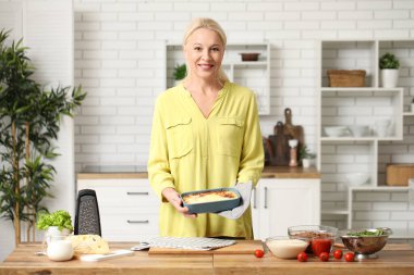 Güzel, olgun, mutlu bir kadın mutfakta lezzetli lazanyayla yemek tabağı tutuyor.