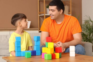 Küçük çocuk ve babası evdeki masada küplerle oynuyorlar.