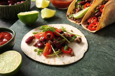 Arka plan olarak yeşil mermer tepside taze taco ve malzemeler var.