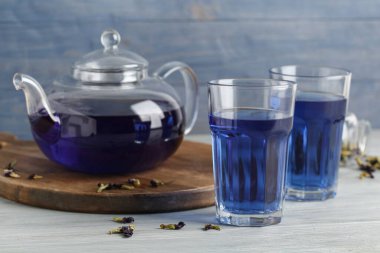 Bardaklar ve çaydanlıklar mavi ahşap arka planda bezelye çiçeği çayı