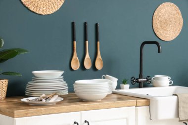 Lavabo ve ahşap masa. Mutfakta mavi duvarın yanında farklı tabaklar var.