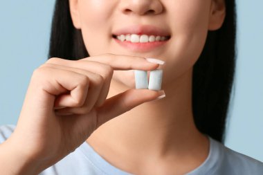 Mavi arka planda diş eti çiğneyen güzel bir Asyalı kadın. Yakın plan.