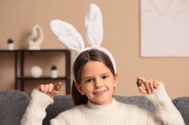 Oturma odasında çikolata yumurtalı tavşan kulaklı şirin bir kız.