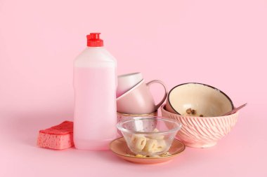 Kirli tabaklar, deterjan ve pembe arka planda sünger.