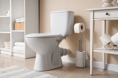 Tuvalet kâsesi ve masa. Tuvalet kağıdı ruloları. Banyoda bej duvarın yanında.