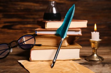 Ahşap zemin üzerinde kalem, mürekkep hokkası, bardak ve kağıt çarşaf olan eski kitaplar.