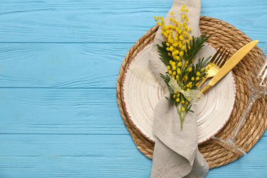 Altın çatal bıçak takımı ve mavi ahşap arka planda mimoza çiçekleri olan güzel bir masa.