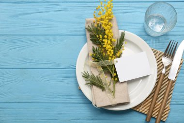 Boş bir kart ve mavi ahşap arka planda mimoza çiçekleri olan güzel bir masa.