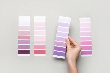 Gri arkaplanda menekşe rengi palet örnekleri olan kadın elleri. Üst görünüm