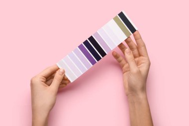 Pembe arka planda menekşe rengi palet örnekleri olan kadın elleri. Üst görünüm