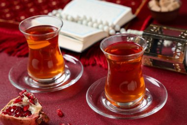 Kırmızı zemin üzerinde Kur 'an, fanatikler ve nar bulunan bir bardak lezzetli Türk çayı. Ramazan kutlaması