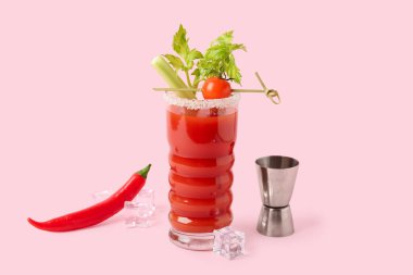 Bir bardak Bloody Mary kokteyli, kereviz, kırmızı biber ve pembe arka planda buz.