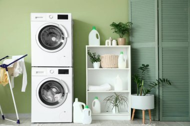 Çamaşır makineleri, raf ünitesi ve katlama ekranlı çamaşır odasının içi.