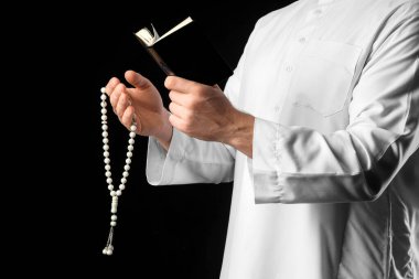 Kuran ve Tasbih 'li Müslüman bir adam siyah arka planda dua ediyor, yakın plan. Ramazan kutlaması