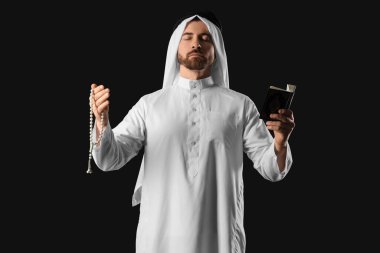 Kuran ve tasbih 'li genç Müslüman adam siyah arka planda dua ediyor. Ramazan kutlaması