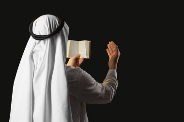 Kuran okuyan genç Müslüman adam siyah arka planda dua ediyor. Ramazan kutlaması