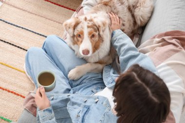 Evde bir fincan çay ve sevimli bir köpekle genç bir kadın.