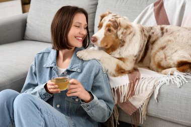 Evdeki kanepenin yanında yeşil çay ve şirin bir köpekle mutlu genç bir kadın.