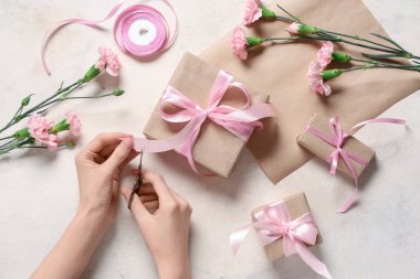 Hediye kutuları, pembe karanfiller ve bej rengi grunge arka planda kurdele kesen kadın elleri. Uluslararası Kadınlar Günü