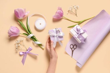 Hediye kutuları, çiçekler ve açık sarı arka planda ambalaj kağıdı olan kadın elleri. Uluslararası Kadınlar Günü